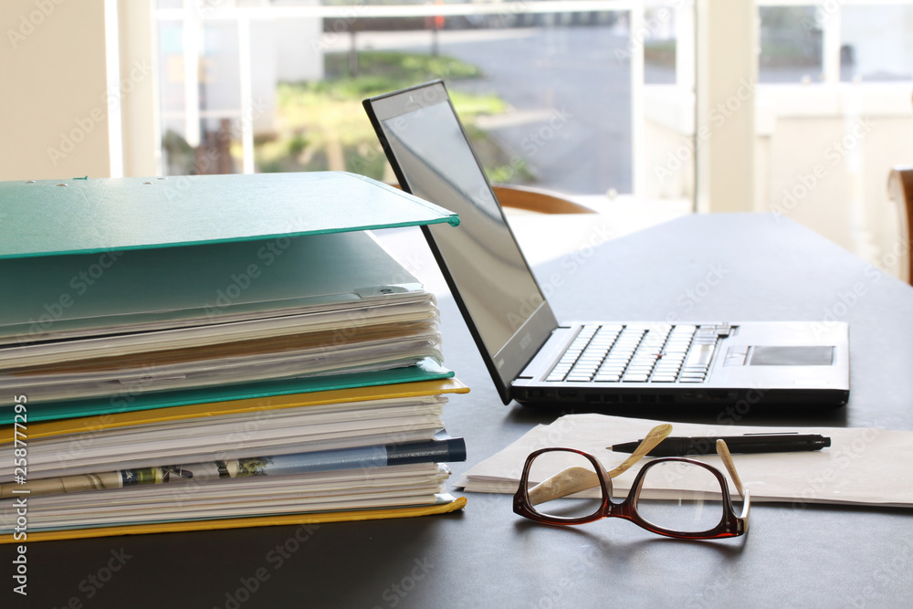 Laptop computer, ring binders filled with papers, glasses, paper sheets and pencil on office table. Selective focus Laptop computer, ring binders filled with papers, glasses, paper sheets and pencil on office table. Selective focus
