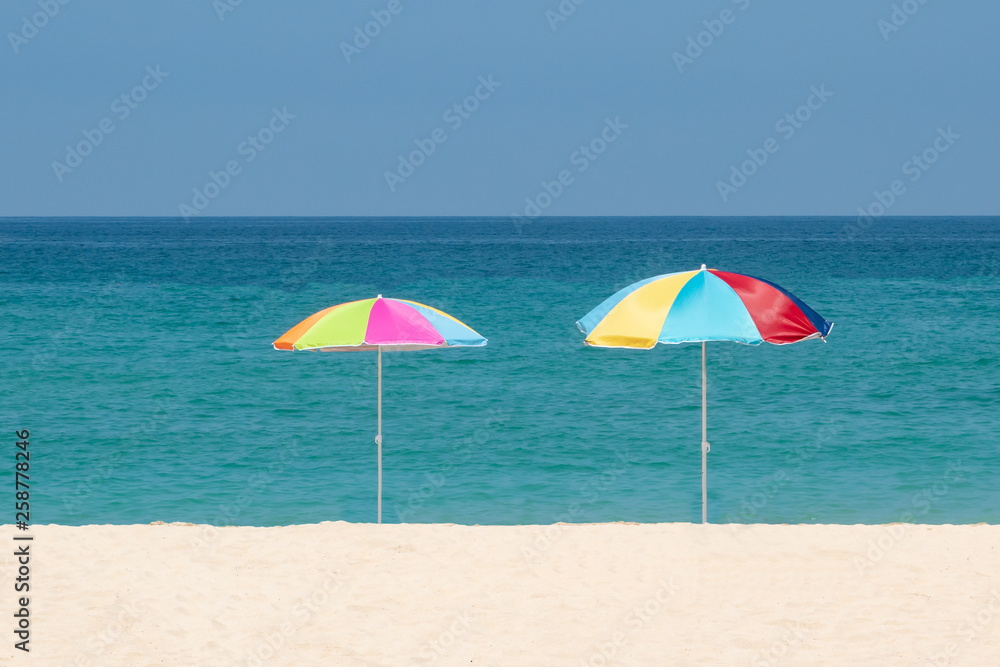 Two parasols on the beach.Multicolored umbrellas on a white sand.Tropical paradise bay,ocean water and blue sky.Concept of relax, summertime,holidays,decorations.
