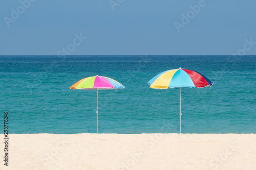 Two parasols on the beach.Multicolored umbrellas on a white sand.Tropical paradise bay,ocean water and blue sky.Concept of relax, summertime,holidays,decorations. © ELENA