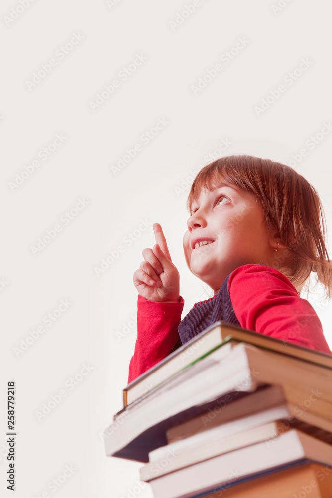 Little cute child girl pointing with finger up on the stack of books as symbol of education, studies and self development. Little cute child girl pointing with finger up on the stack of books as symbol of education, studies and self development.