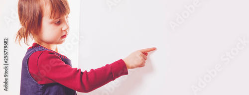 Llittle cute child girl pointing to a white board. Space for text.