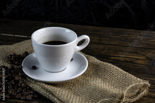 Cup of coffee and coffee beans on a rough wooden background.