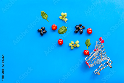 Online shopping concept with trolley near producs on blue background top view mock up photo