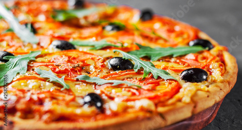 Pizza with Mozzarella cheese, Tomatoes, pepper, olive, Spices and Fresh arugula. Italian pizza. Pizza Margherita or Margarita on Dark grey black slate background