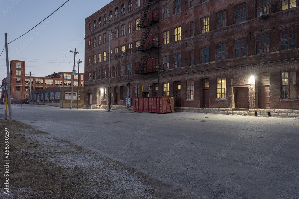 Down an industrial street behind a vintage multiple story red brick warehouse with lights