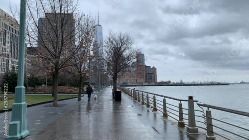 Man walks dog in Hudson River Park on rainy afternoon with freedom tower in background_USA