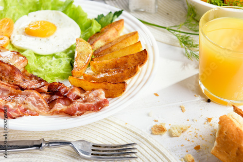 Morning breakfast with delicious fried bacon, French fries and tender egg, close-up.