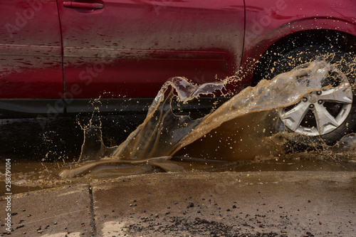 Canvas Print Vehicle driving through pothole splashing muddy water.