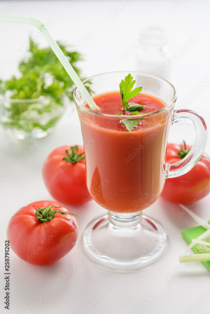 Tomato juice is poured into a transparent glass with parsley and herring, on a white background with cherry tomatoes, lit by sunlight Tomato juice is poured into a transparent glass with parsley and herring, on a white background with cherry tomatoes, lit by sunlight