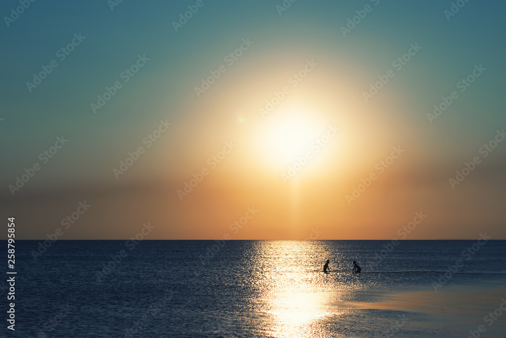  Children bathe in the sea in the evening at sunset. Sunset on the beach. Bright sunset against the sky and the sea. Beautiful sunset over a calm ocean or sea.