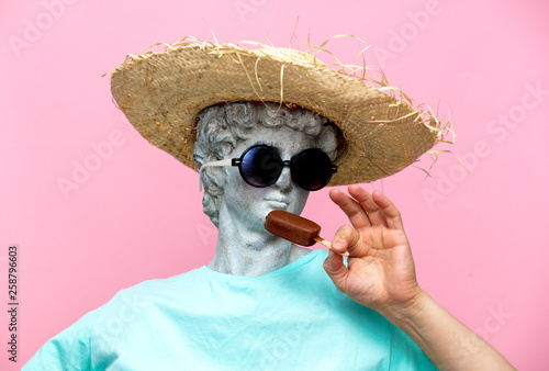 Obraz na plátně Antique bust of male in hat with ice-cream on pink background.