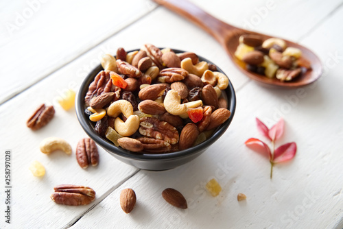 Mix nuts and dried fruits background and wallpaper. Seen in top view of mix nuts and dried fruits in the bowl and wood spoon decorated with some nuts and red leaf on white wood in background.
