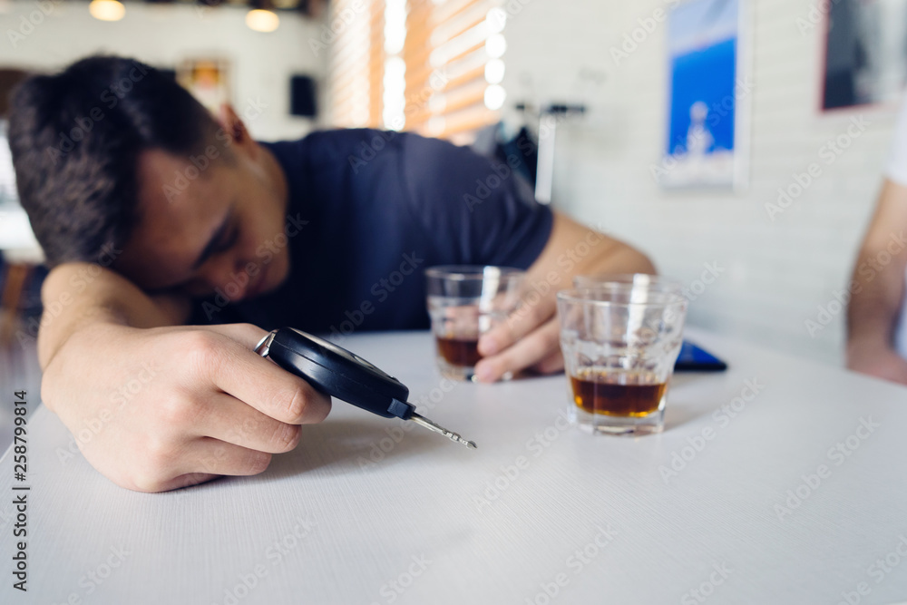 Drunk man sleeping on table at cafe with car keys and whiskey in hand driving and drinking alcohol Drunk man sleeping on table at cafe with car keys and whiskey in hand driving and drinking alcohol