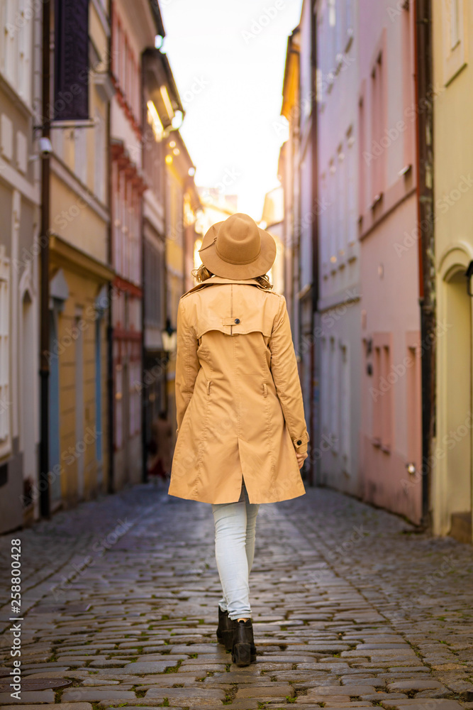 Girl in a beige hat and coat in narrow street of Prague city, Czech Republic