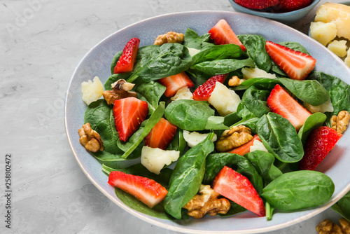 salad with strawberry, spinach leaves, parmesan cheese and walnuts on concrete background. healthy diet food