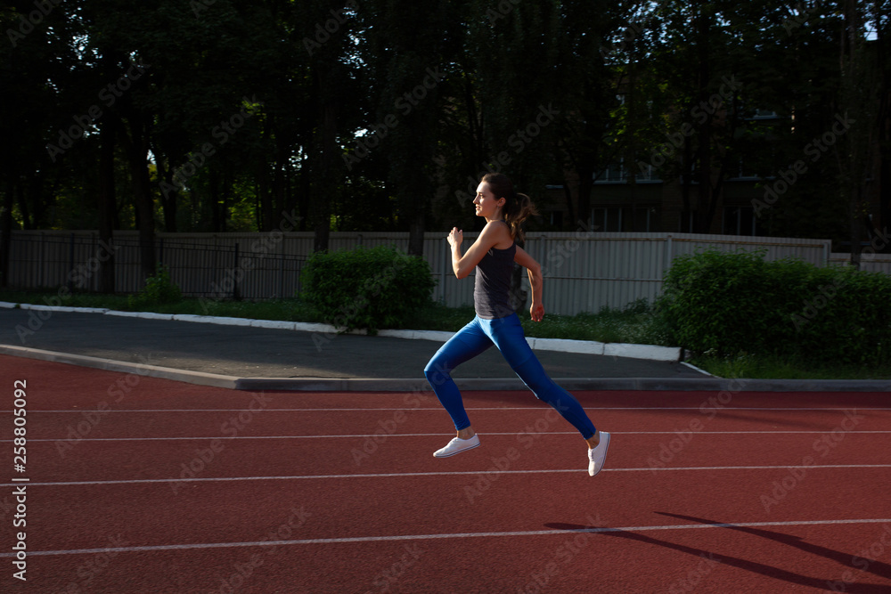 Athletic girl wearing sport apparel running at the empty stadium at the evening. Space for text