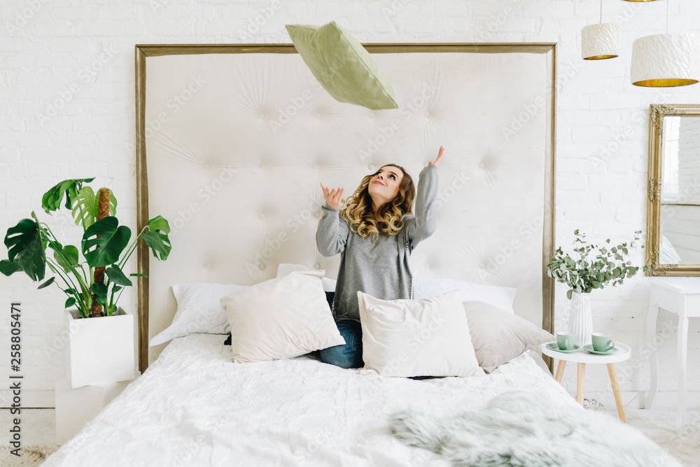 Naklejka premium Beautiful young caucasian European woman having fun throwing pillow in the air at home