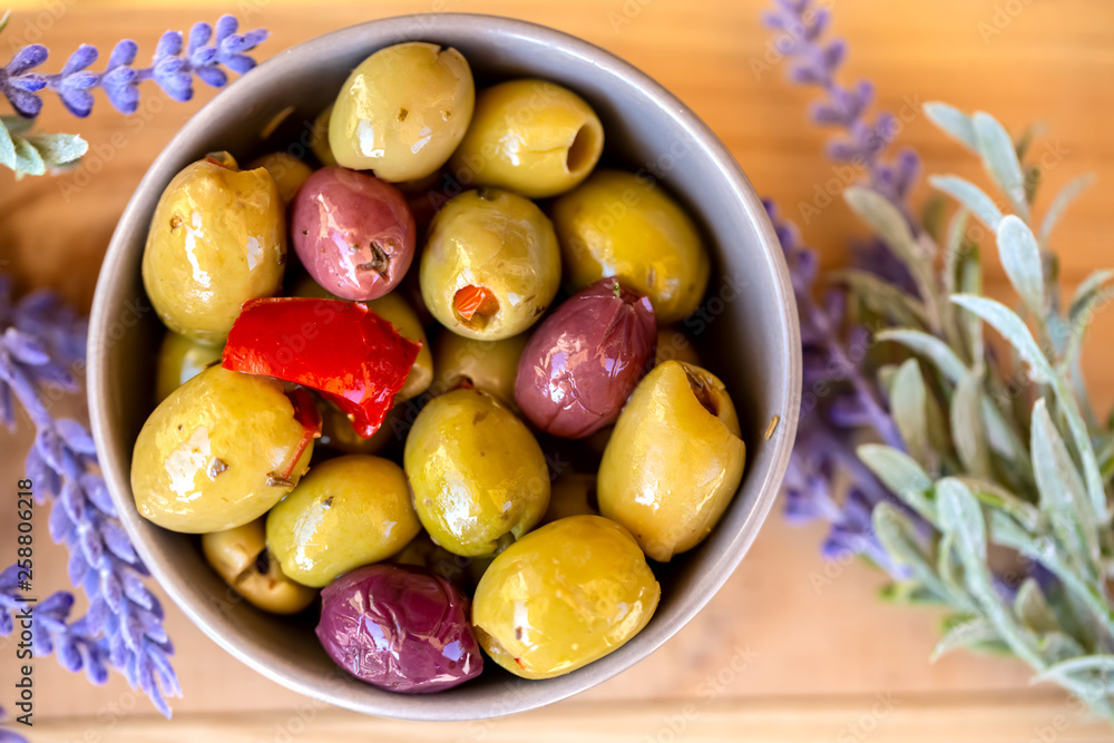 Olives stuffed with red pepper and herbs spices. Multi-colored olives in a small bowl on a wooden table. Lavender. Blurry background. Close up. Soft focus. Top view.