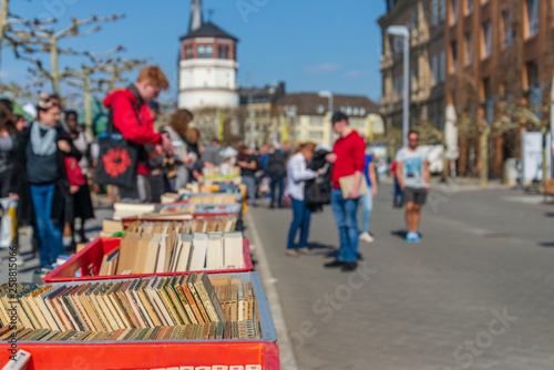 Tela Selected focus on stack of books, outdoor sunny view of people attend on open air book festival at promenade along riverside of Rhine River in Spring season in Düsseldorf, Germany