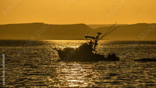 A fishing boat in silhouette in a bay at sunset moving back to port.