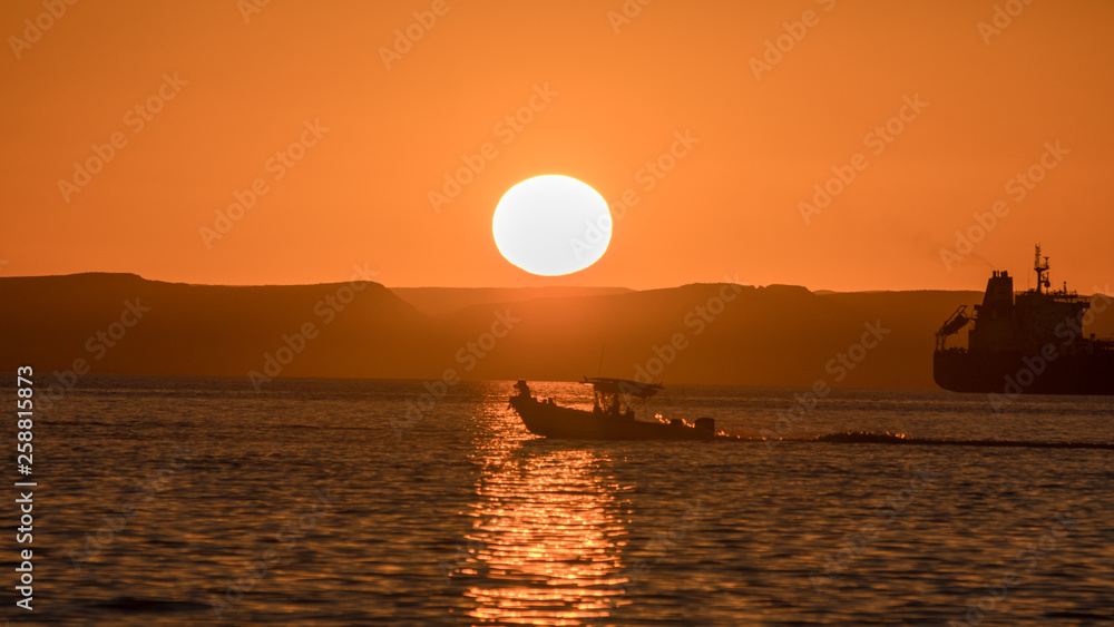 silhouette of a small fishing boat crossing the bay with sun behind it.