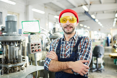 Waist up portrait of mature bearded man working at factory and posing confidently standing in industrial workshop, copy space