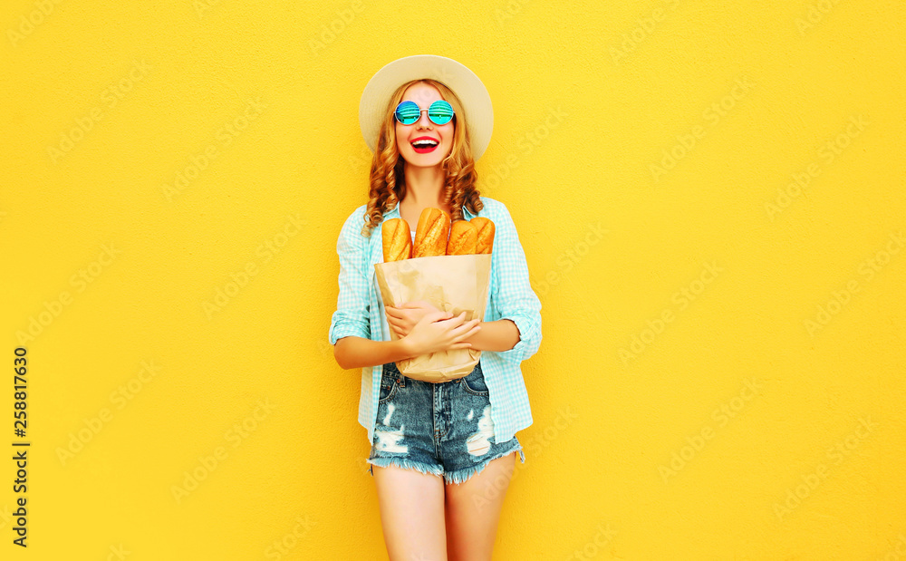 portrait happy laughing young woman holding paper bag with long white bread baguette, wearing straw hat, shorts on colorful yellow background portrait happy laughing young woman holding paper bag with long white bread baguette, wearing straw hat, shorts on colorful yellow background