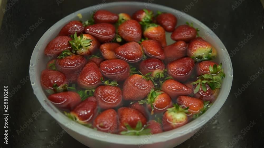 Bowl with strawberries soaked in water to clean the dirt fruit with man's hand picking some. Bowl with strawberries soaked in water to clean the dirt fruit with man's hand picking some.