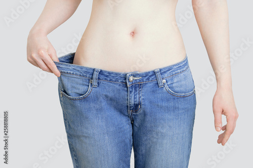 The concept of diet and weight loss. Woman in big jeans on pastel gray background © Iuliia Alekseeva