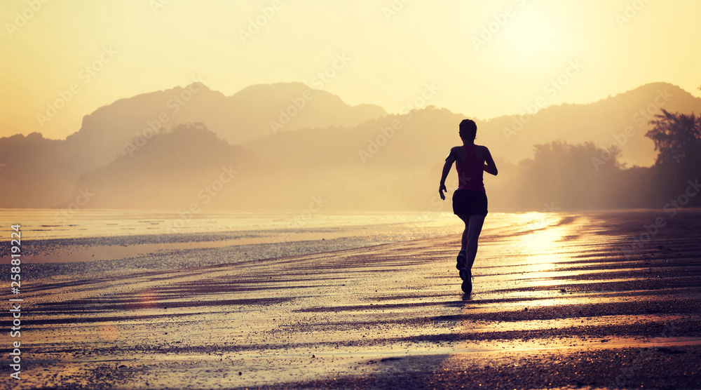 Silhouette of young fitness woman running at sunrise beach