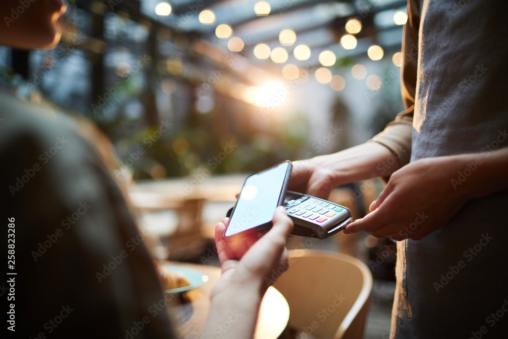 © Seventyfour - Close-up of unrecognizable woman using modern gadget while making online payment in cafe, nfc technology concept