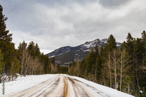 Two lane road with Rocky Mountains snow covered peaks in background, Estes Park, Colorado
