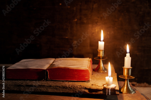 A bible open on a table next to a candle. The light illuminating the bible is only from the candle. Perfect for religion, easter and christmas themes.