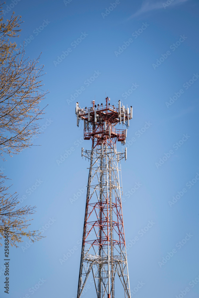 A tall metal cellular tower with a tree set on a clear blue sky background.