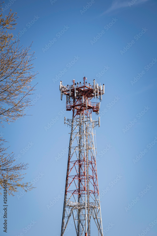 A tall metal cellular tower with a tree set on a clear blue sky background. A tall metal cellular tower with a tree set on a clear blue sky background.