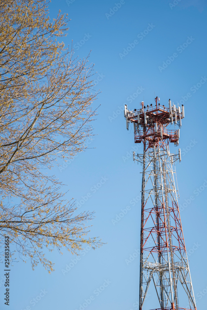 A tall metal cellular tower with a tree set on a clear blue sky background. A tall metal cellular tower with a tree set on a clear blue sky background.