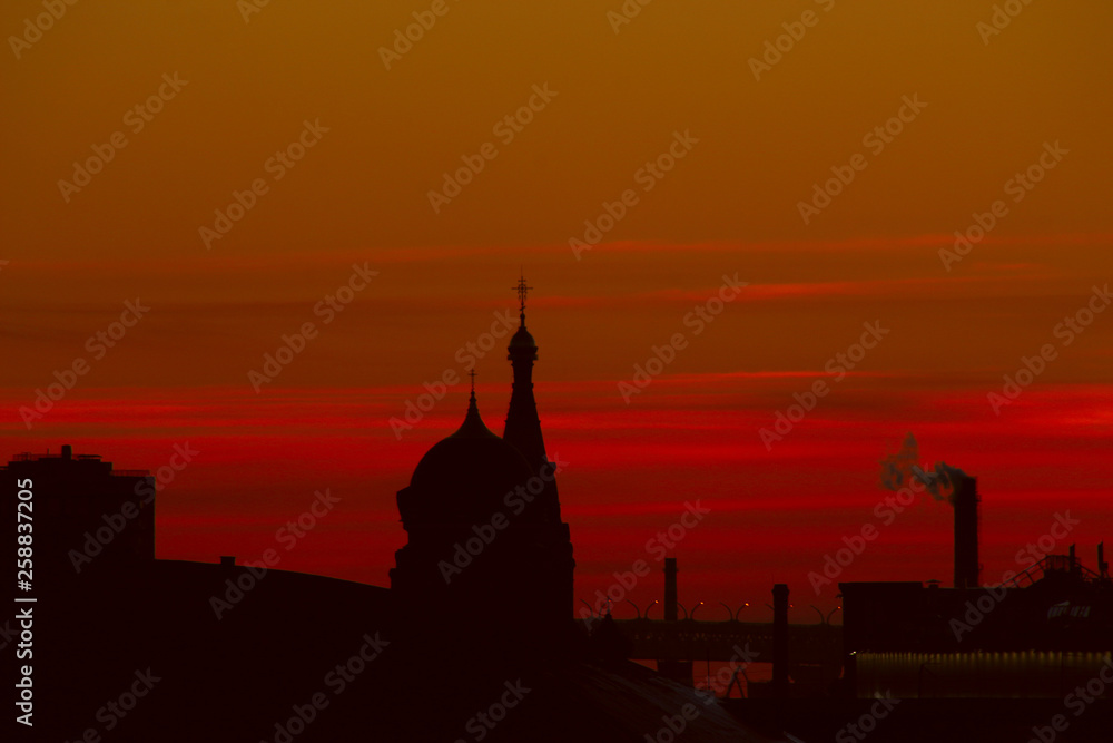 cityscape: silhouettes of churches, industrial pipes and city roofs at sunset