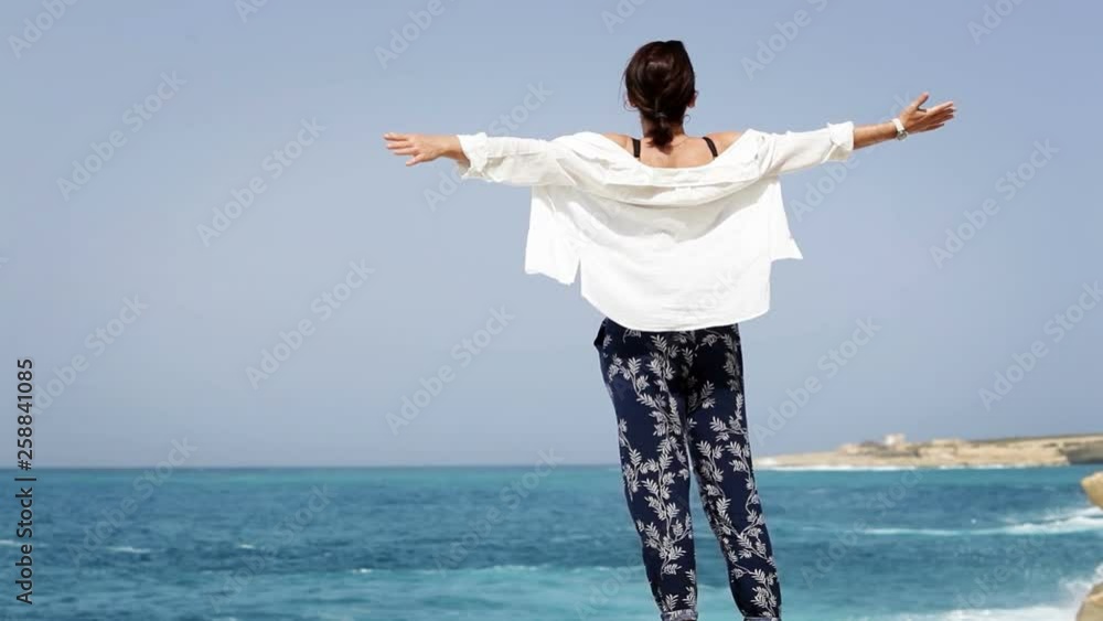 Girl standing on seashore with arms open wide and looking at waves Girl standing on seashore with arms open wide and looking at waves