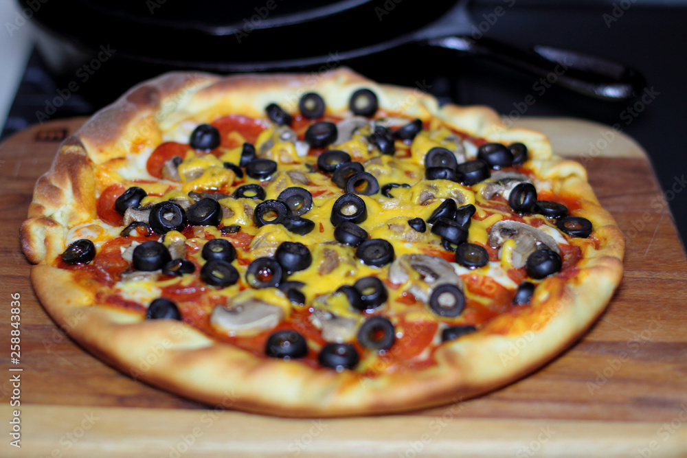 Freshly baked homemade pizza with pepperoni, mushrooms, and black olives in cast iron pan from the oven. Freshly baked homemade pizza with pepperoni, mushrooms, and black olives in cast iron pan from the oven.
