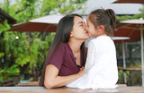 Adorable little Asian child girl kissing her mother with love near a glass window with water drop while raining day.