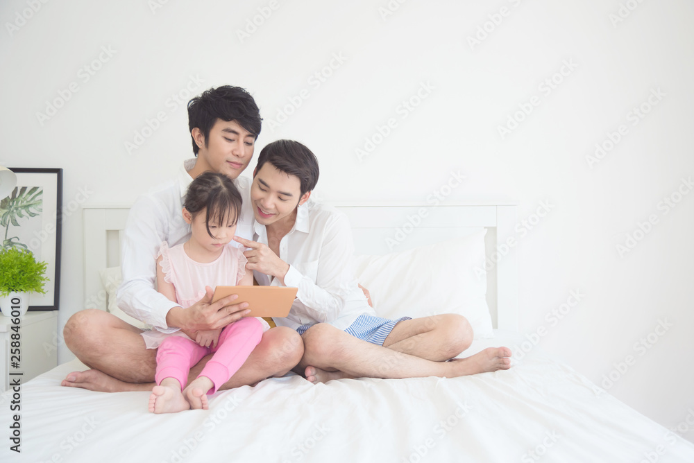 Asian Male gay couple using tablet with their daughter in bedroom Asian Male gay couple using tablet with their daughter in bedroom