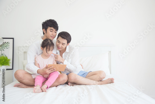 Asian Male gay couple using tablet with their daughter in bedroom