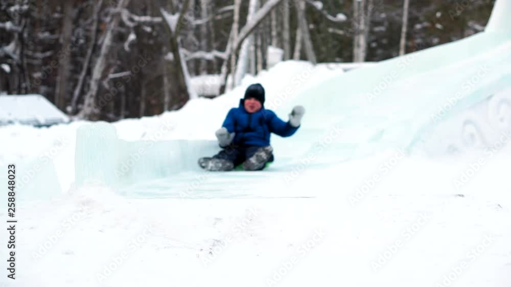 Boy sledging down the hill at winter park. Ice slide in the recreation Park in winter Boy sledging down the hill at winter park. Ice slide in the recreation Park in winter
