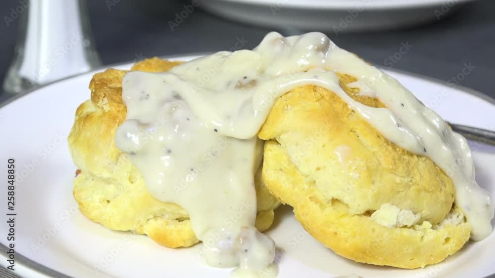 Spooning country gravy with sausage bits onto hot biscuits Spooning country gravy with sausage bits onto hot biscuits