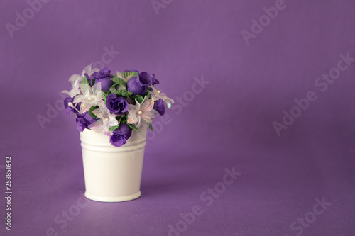 Pink and purple flowers in a white bucket on a purple background with copy space
