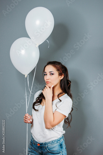 Beautiful sad asian young woman with dark long hair with white balloons isolated on grey background