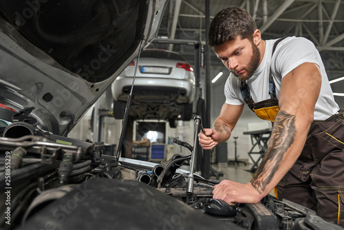 Strong man wearing coveralls repairing engine in automobile