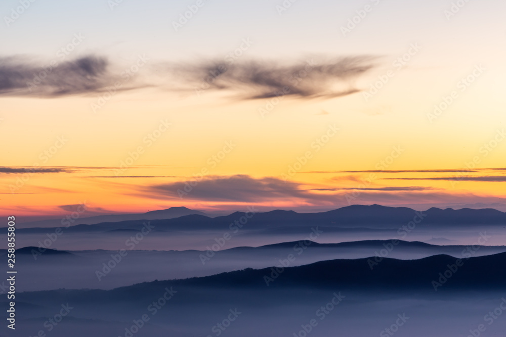Beautifully colored sky at dusk, with mountains layers and mist between them