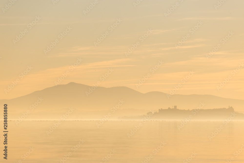 Beautiful view of Trasimeno lake at sunset with birds on water and Castiglione del Lago town Beautiful view of Trasimeno lake at sunset with birds on water and Castiglione del Lago town
