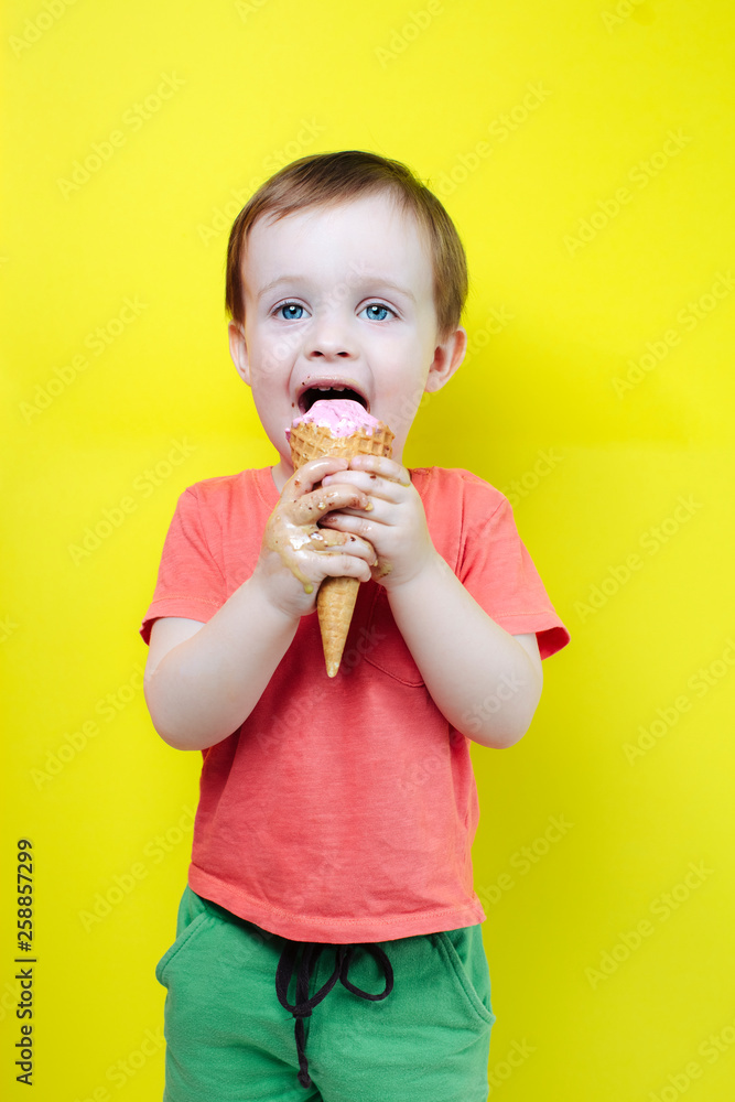 Laughing boy with eyes wide open and mouth eating ice cream cones stay along on bright colorful background wall, have summer mood and laugh. Laughing boy with eyes wide open and mouth eating ice cream cones stay along on bright colorful background wall, have summer mood and laugh.